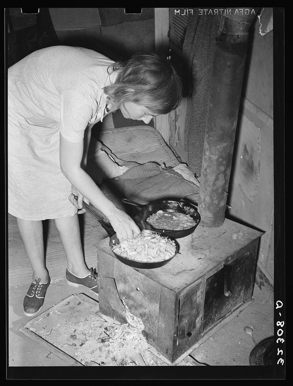 En svartvit vintagebild som visar en kvinna i 1940-talskläder som tar ut pajer ur en vedeldad ugn.