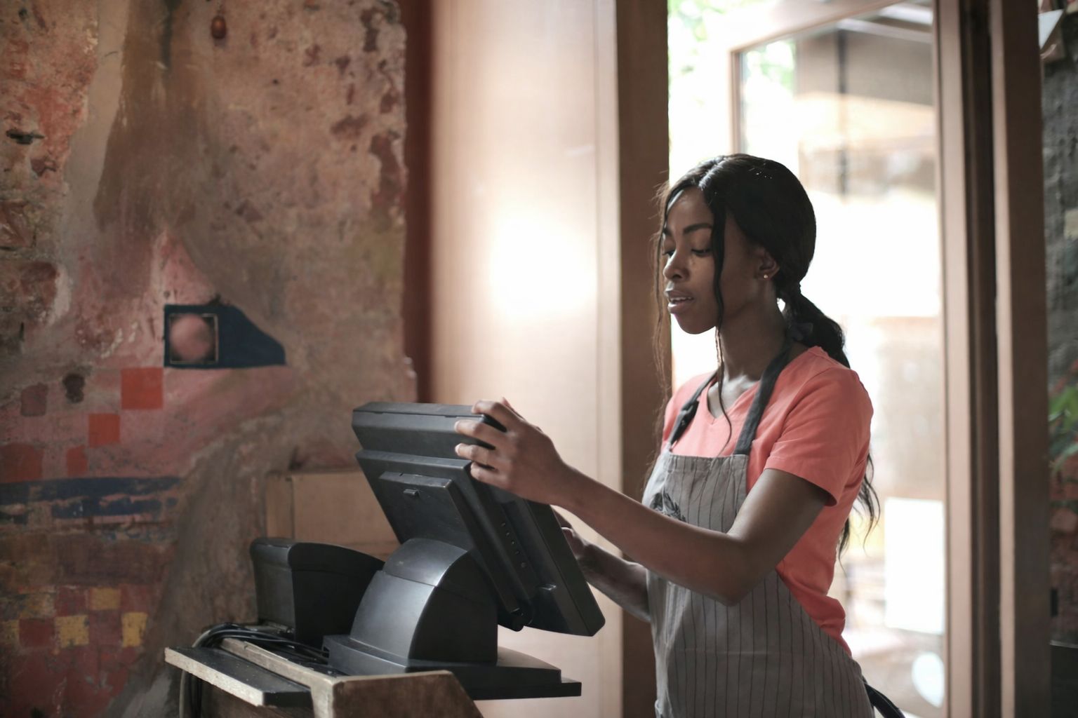 En kvinna i förkläde vid en kassaterminal, med fokus på handel och finansiering.